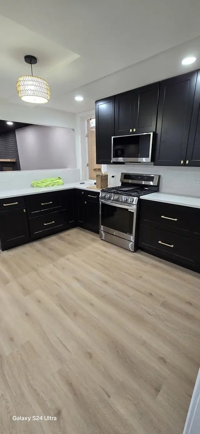 Kitchen with black cabinets, brass pulls, white countertops, a stainless gas range and wood-look floor