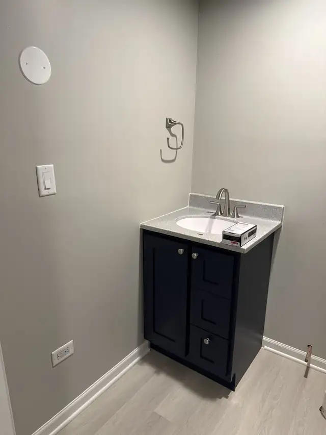 Black half bath vanity with a white top, chrome faucet and towel ring on a fresh grey wall